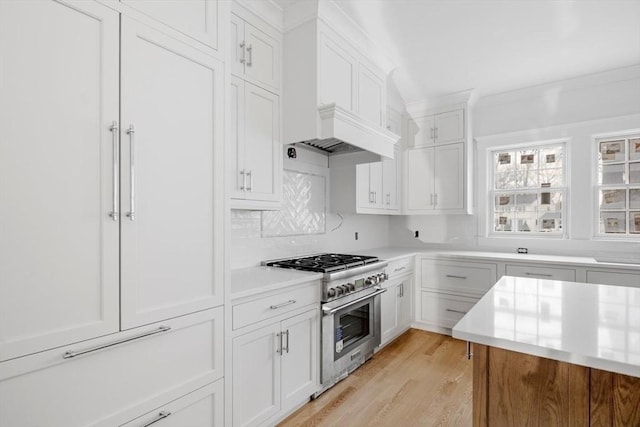 kitchen with stainless steel stove, white cabinetry, ornamental molding, light hardwood / wood-style floors, and custom range hood