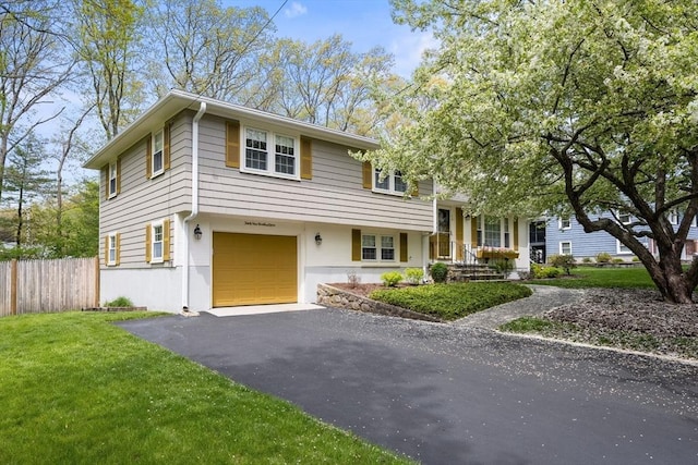 split level home featuring aphalt driveway, fence, an attached garage, and a front yard