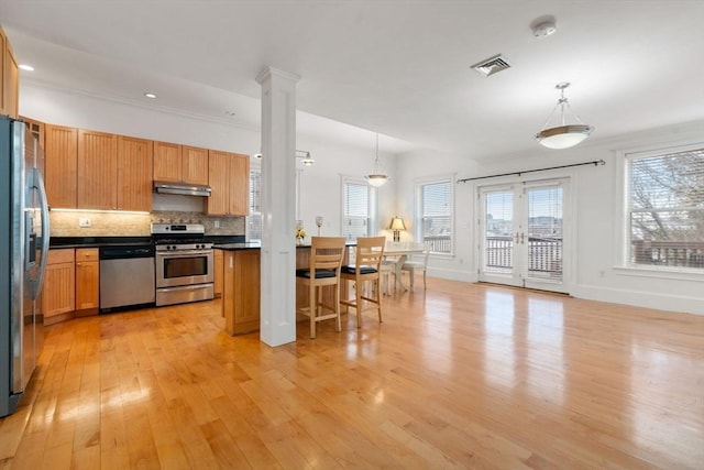 kitchen with backsplash, hanging light fixtures, stainless steel appliances, and light wood-type flooring