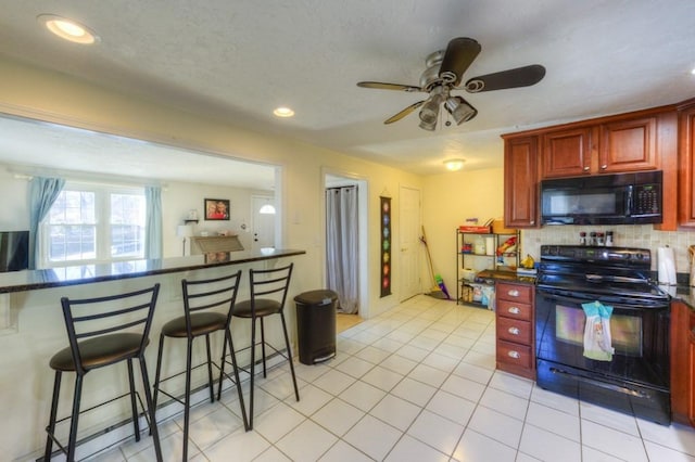 kitchen with a kitchen breakfast bar, black appliances, light tile patterned floors, ceiling fan, and decorative backsplash