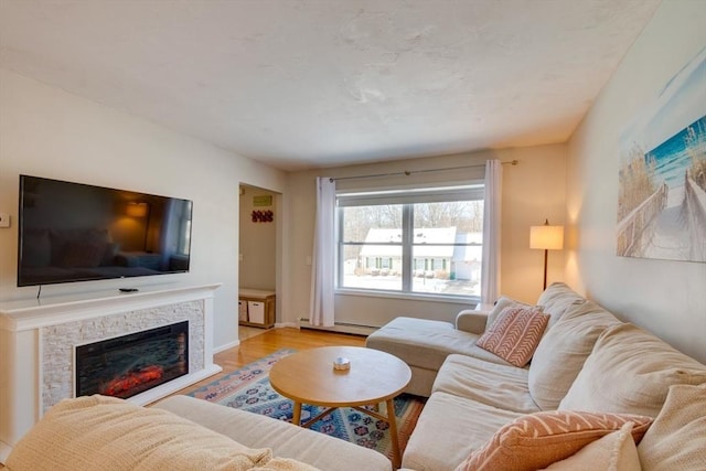 living room featuring baseboard heating, a stone fireplace, and light hardwood / wood-style flooring