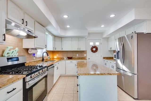 kitchen with sink, white cabinetry, stainless steel appliances, a center island, and light stone counters