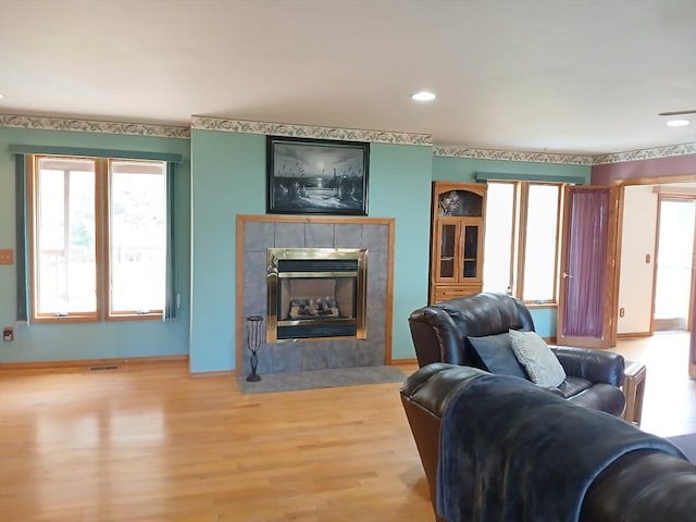 living area with a fireplace, light wood-style flooring, visible vents, and plenty of natural light