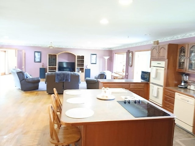 kitchen featuring light countertops, black appliances, a kitchen bar, glass insert cabinets, and open floor plan