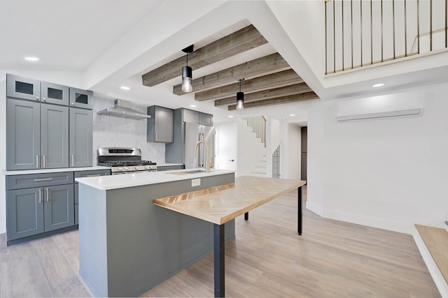 kitchen with appliances with stainless steel finishes, pendant lighting, a wall unit AC, beam ceiling, and light hardwood / wood-style flooring