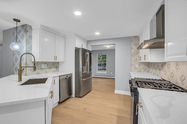 kitchen with wall chimney exhaust hood, sink, hanging light fixtures, appliances with stainless steel finishes, and white cabinets