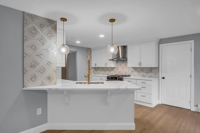 kitchen with white cabinetry, wall chimney range hood, decorative light fixtures, and kitchen peninsula