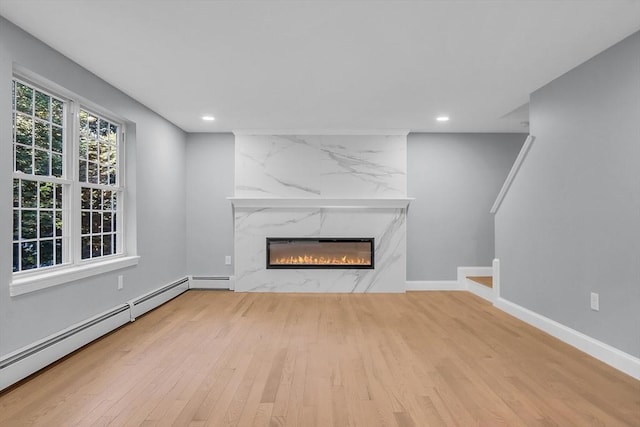 unfurnished living room featuring a baseboard radiator, a high end fireplace, and light hardwood / wood-style floors