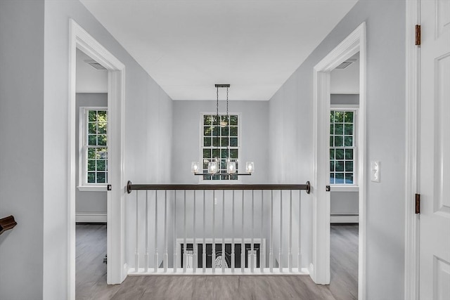 hall featuring baseboard heating, a healthy amount of sunlight, an inviting chandelier, and hardwood / wood-style floors