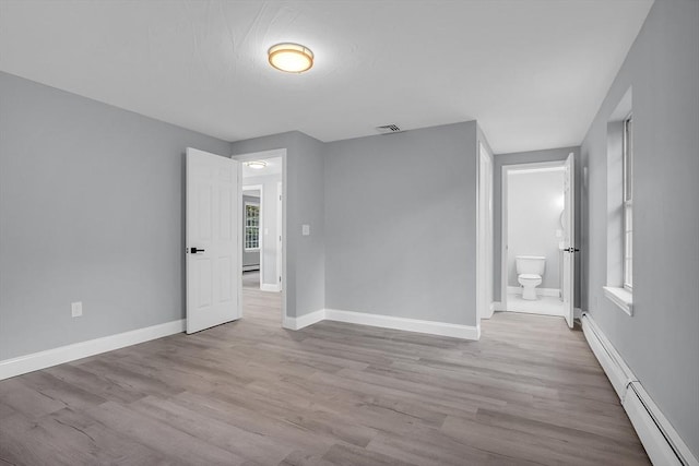 unfurnished bedroom featuring ensuite bathroom, a baseboard heating unit, and light wood-type flooring