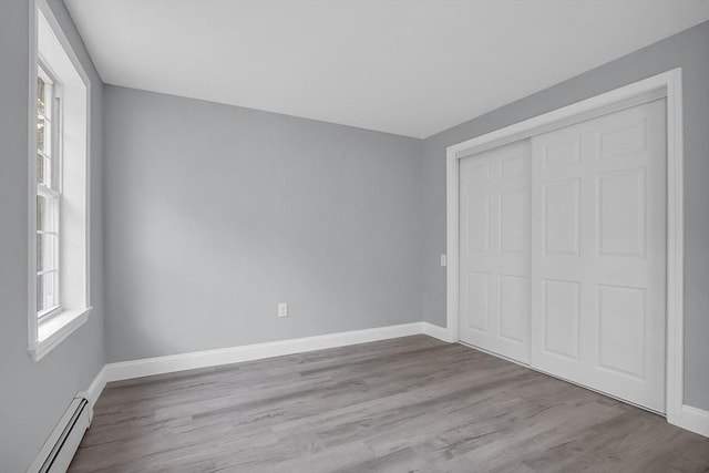 unfurnished bedroom with a baseboard radiator, light hardwood / wood-style floors, and a closet