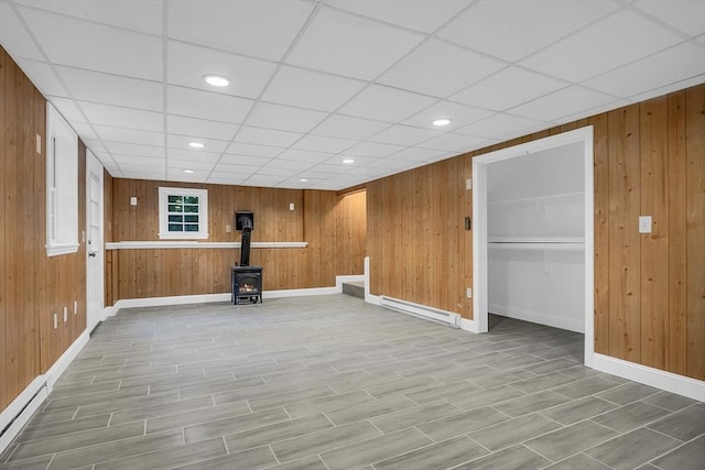 basement with a baseboard heating unit, a wood stove, and wood walls