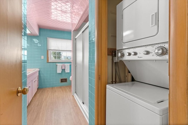 laundry room featuring light wood-style flooring, stacked washer and dryer, laundry area, visible vents, and tile walls