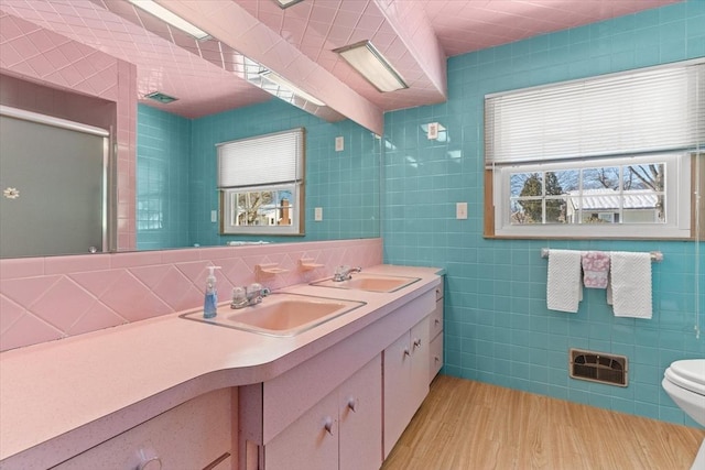 full bathroom with wood finished floors, a sink, tile walls, and double vanity