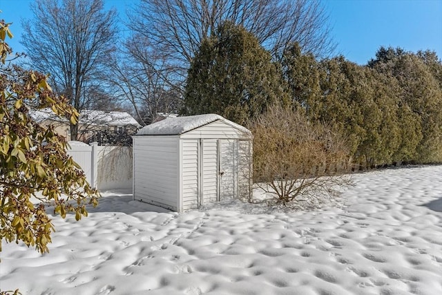 snow covered structure with an outbuilding, fence, and a shed