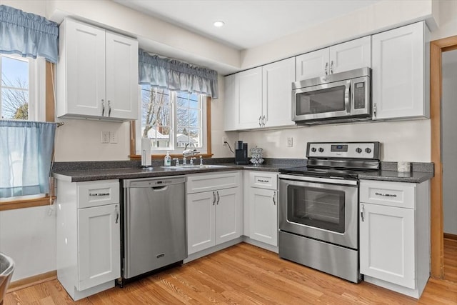 kitchen with white cabinets, dark countertops, appliances with stainless steel finishes, light wood-type flooring, and a sink