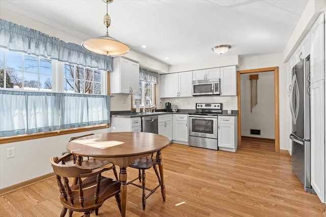 kitchen with dark countertops, light wood-style flooring, appliances with stainless steel finishes, white cabinetry, and pendant lighting