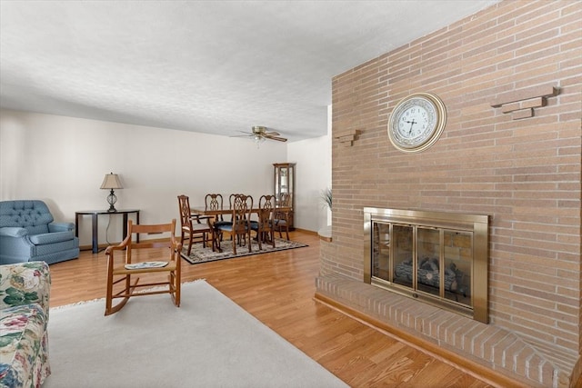 living room featuring a ceiling fan, a fireplace, and wood finished floors