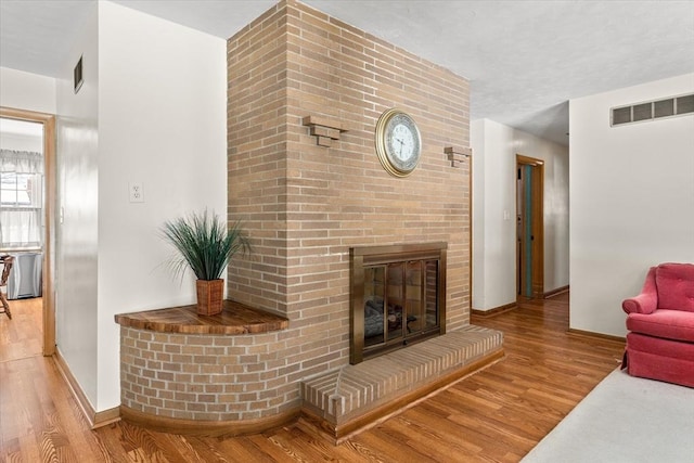 living room featuring light wood-style floors, visible vents, a fireplace, and baseboards