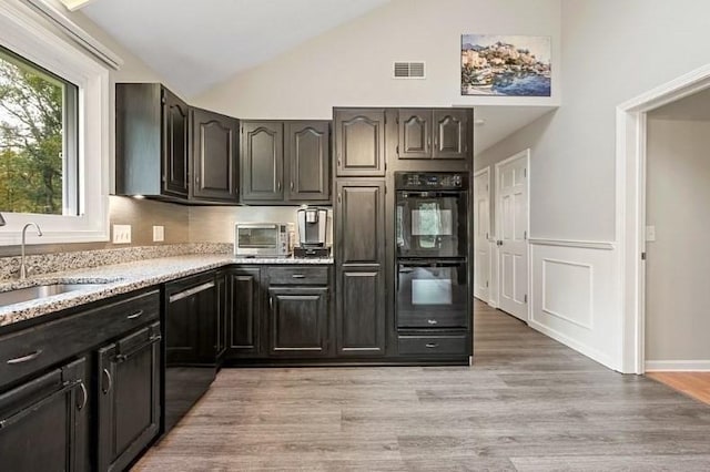 kitchen with light wood-type flooring, light stone counters, black appliances, sink, and high vaulted ceiling