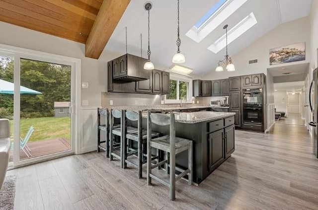 kitchen with beam ceiling, a skylight, double oven, a breakfast bar area, and dark brown cabinets