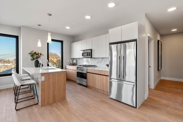 kitchen featuring light hardwood / wood-style floors, appliances with stainless steel finishes, white cabinetry, decorative backsplash, and decorative light fixtures