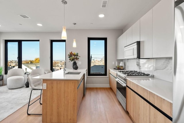 kitchen featuring hanging light fixtures, a kitchen island with sink, white cabinets, sink, and high end stainless steel range