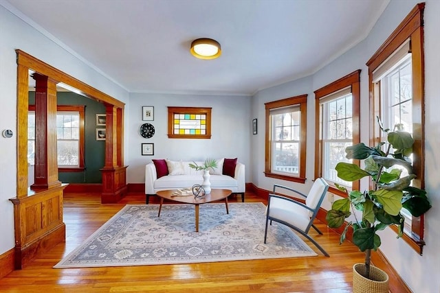 sitting room with ornate columns, light wood-style flooring, baseboards, and crown molding