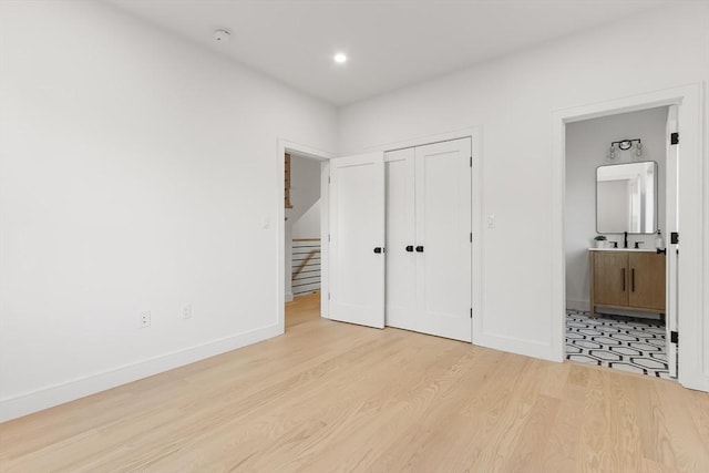 unfurnished bedroom with a closet, connected bathroom, a sink, wood finished floors, and baseboards