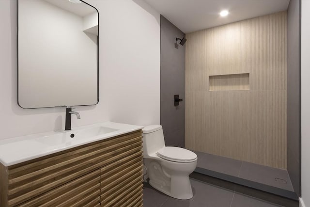 bathroom featuring vanity, tiled shower, tile patterned flooring, and toilet