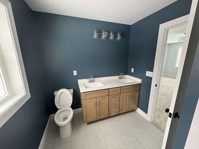 bathroom with toilet, a sink, baseboards, and double vanity