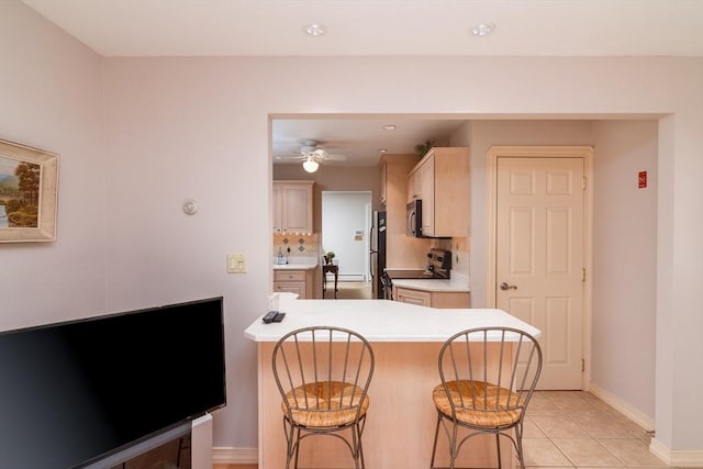 kitchen featuring electric stove, light brown cabinetry, light tile patterned floors, stainless steel refrigerator, and a kitchen breakfast bar