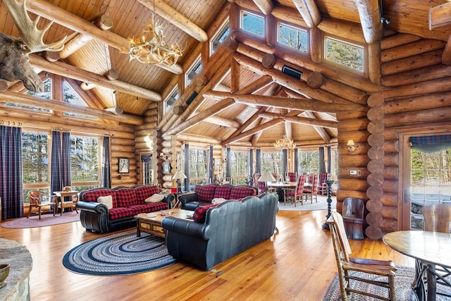 living room featuring a notable chandelier, rustic walls, a wealth of natural light, high vaulted ceiling, and light hardwood / wood-style flooring