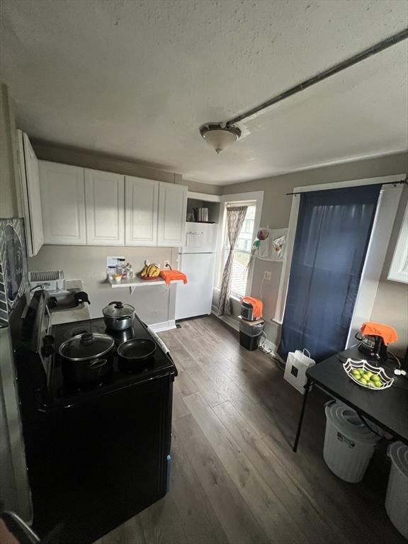 kitchen featuring wood-type flooring, black electric range, white cabinets, and white refrigerator