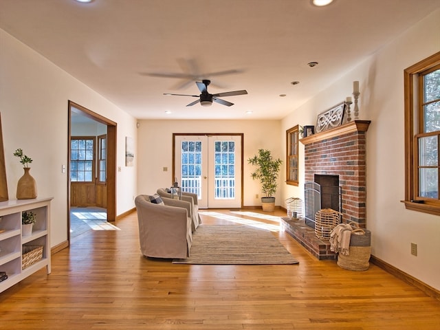 living room with a fireplace, french doors, light wood-type flooring, and ceiling fan