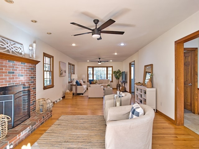 living room featuring light wood-type flooring, a brick fireplace, and ceiling fan