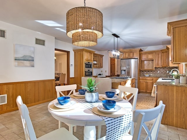 dining space featuring a notable chandelier, wood walls, and sink