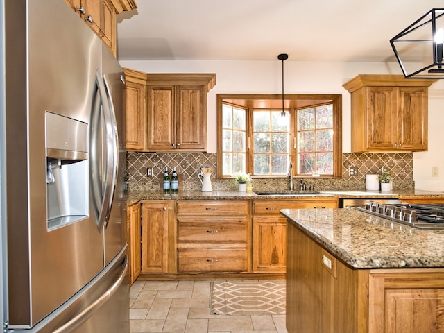 kitchen with light stone countertops, sink, backsplash, stainless steel fridge, and decorative light fixtures