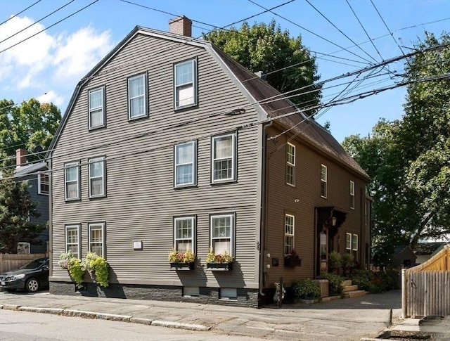 view of property exterior featuring a chimney, fence, and a gambrel roof