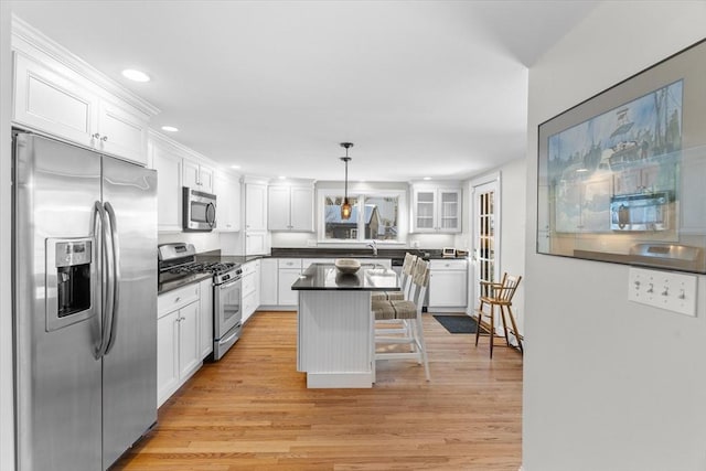 kitchen with stainless steel appliances, dark countertops, hanging light fixtures, white cabinetry, and a kitchen bar