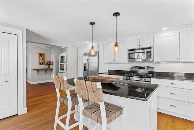 kitchen featuring decorative light fixtures, dark countertops, appliances with stainless steel finishes, white cabinets, and a kitchen island