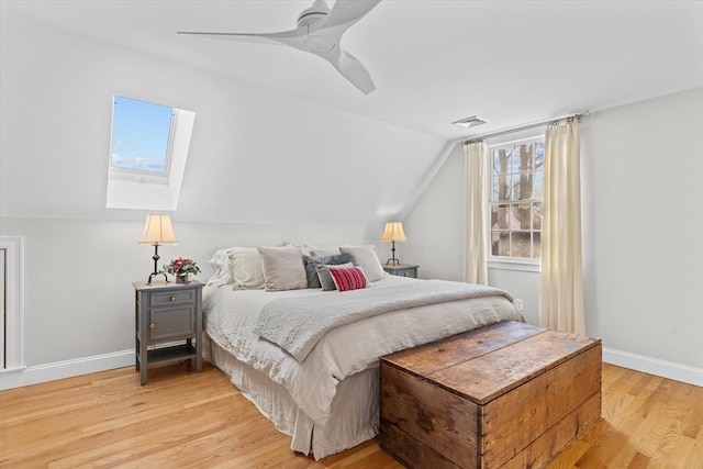 bedroom featuring light wood finished floors, visible vents, a ceiling fan, vaulted ceiling with skylight, and baseboards