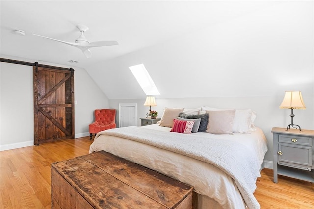 bedroom featuring a barn door, light wood-style floors, lofted ceiling with skylight, ceiling fan, and baseboards