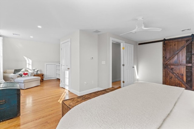 bedroom with visible vents, a barn door, a ceiling fan, wood finished floors, and baseboards