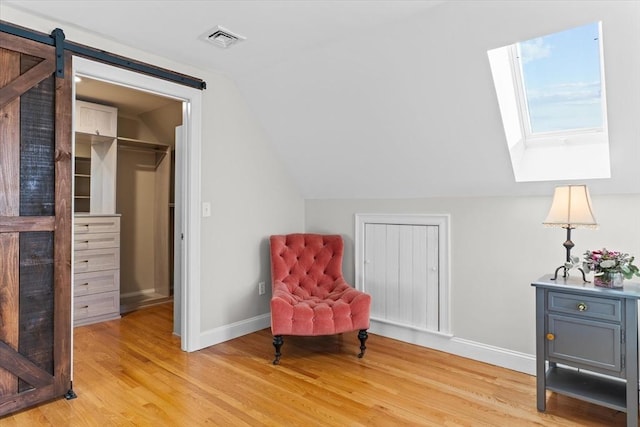 living area featuring vaulted ceiling with skylight, a barn door, light wood-style flooring, visible vents, and baseboards