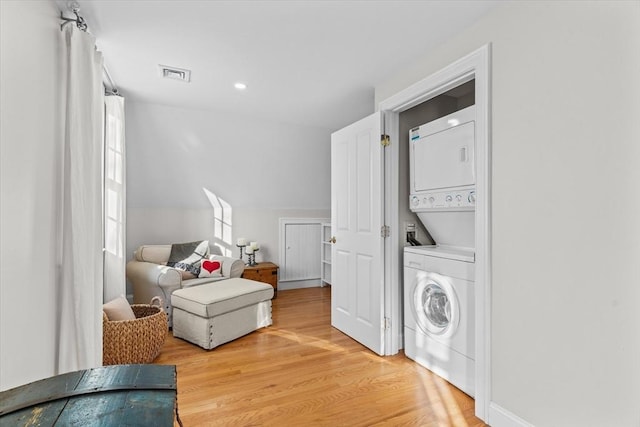 living area with visible vents, wood finished floors, stacked washer and clothes dryer, and lofted ceiling