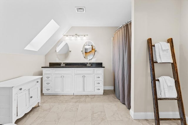 bathroom featuring vaulted ceiling with skylight, marble finish floor, a sink, and double vanity