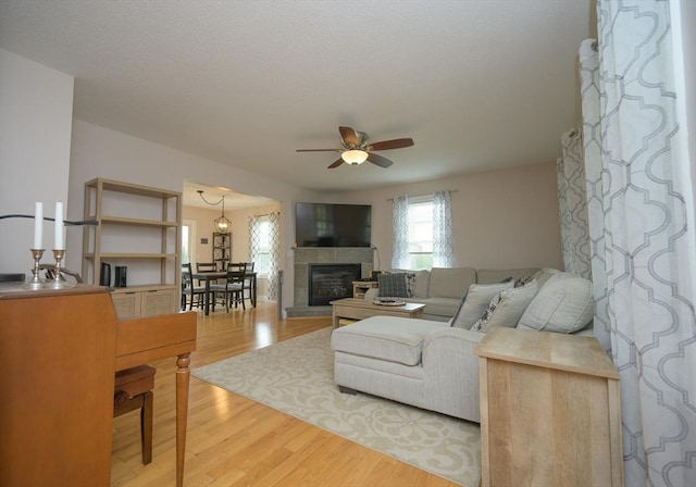 living room featuring light wood-style floors, a ceiling fan, and a tiled fireplace