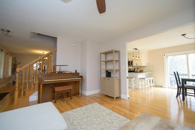living room featuring stairs, a ceiling fan, baseboards, and light wood finished floors