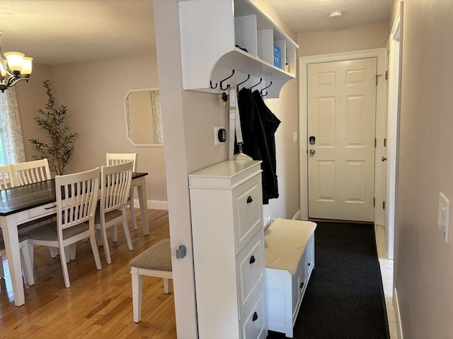 mudroom with light wood-type flooring, a textured ceiling, and a notable chandelier